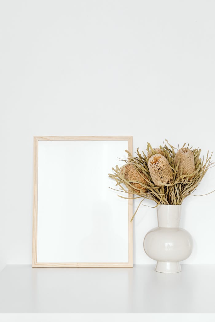 Elegant minimalist mockup featuring a blank picture frame and banksia flowers in a ceramic vase.